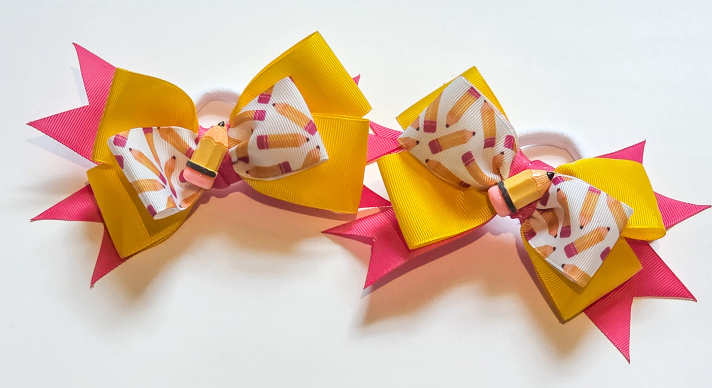 Two matching hair bows on a white background. Each bow features a large yellow ribbon loop, a smaller pink ribbon loop, and a center patterned ribbon with a pencil illustration on a white background.